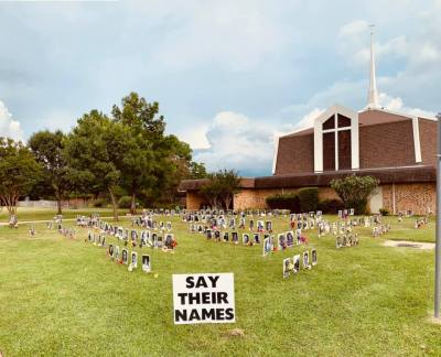 The Say Their Names Memorial displayed on the lawn at a church; black and white headshots with names of Black people killed unjustly, with flowers at each picture